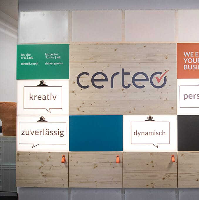 A wall display for Certeo features the logo "certeo" and three illuminated speech bubbles with the words "kreativ," "zuverlässig," and "dynamisch." Additional text panels in German highlight their expertise in B2B procurement.