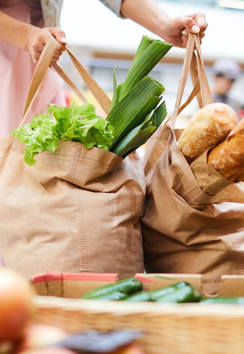 A person places two reusable bags filled with fresh produce and baguettes on a wooden counter in a grocery store, showcasing the convenience of Click&Collect services as a modern retail booster.