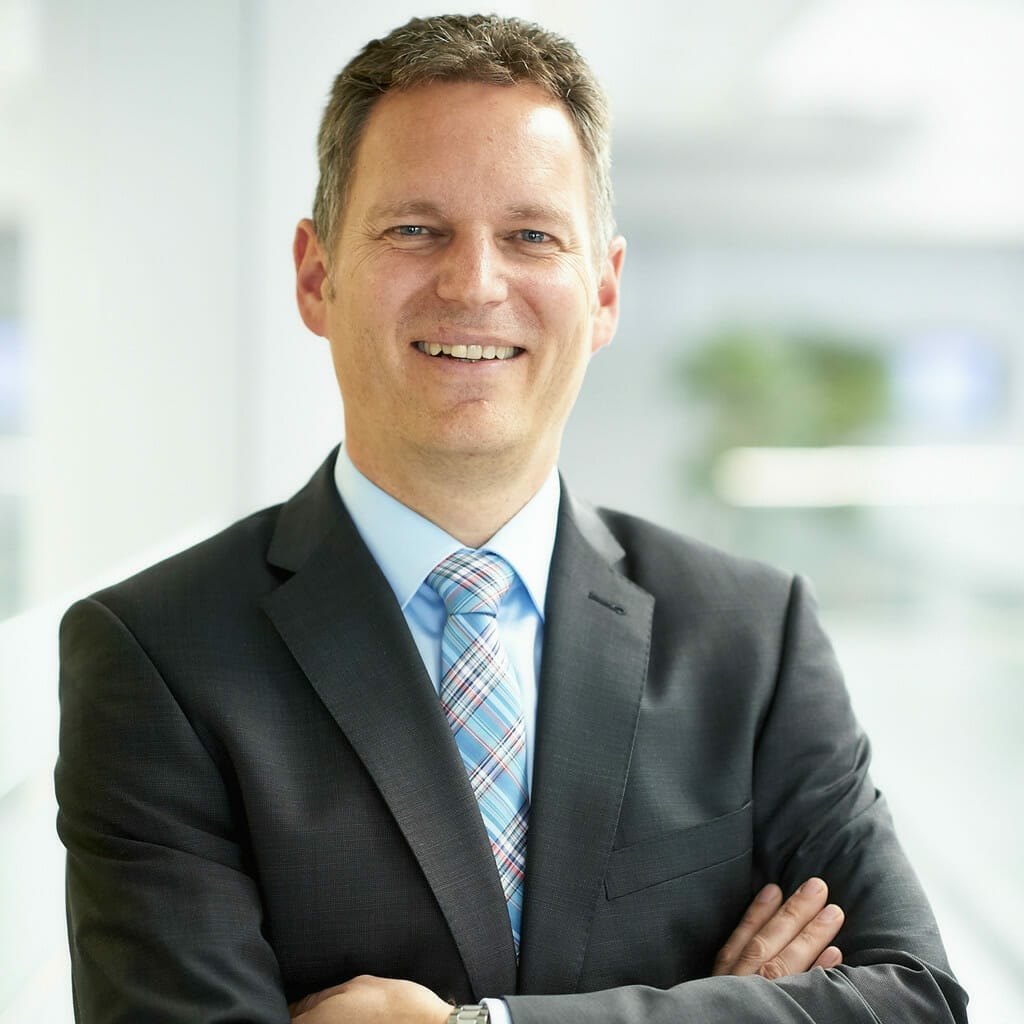 A man wearing a suit and tie stands smiling with folded arms in a bright indoor setting, embodying the confidence and professionalism associated with SEO strategies.