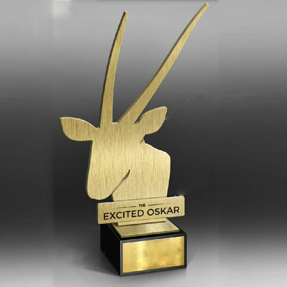 A gold trophy shaped like an antelope head on a black base, with the text "THE EXCITED OSKAR" engraved on a plaque, awaits its place on the main stage.