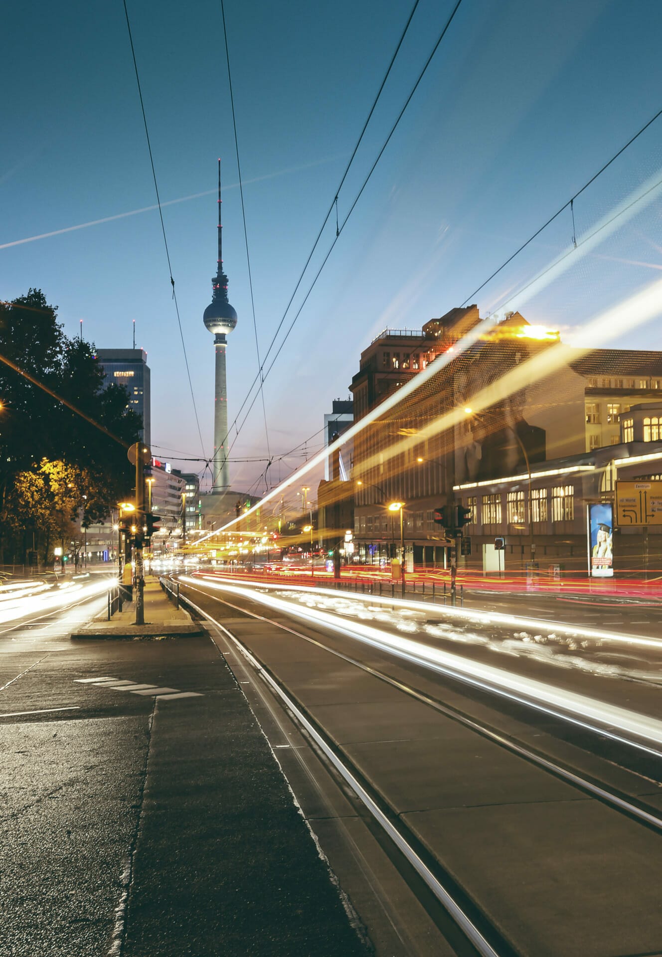 A city street at dusk with light trails from moving vehicles and trams, streetlights, and illuminated buildings. In the distance, a tall tower stands like a beacon of progress amid the urban hustle, reminiscent of a city in the midst of an exciting financing round.