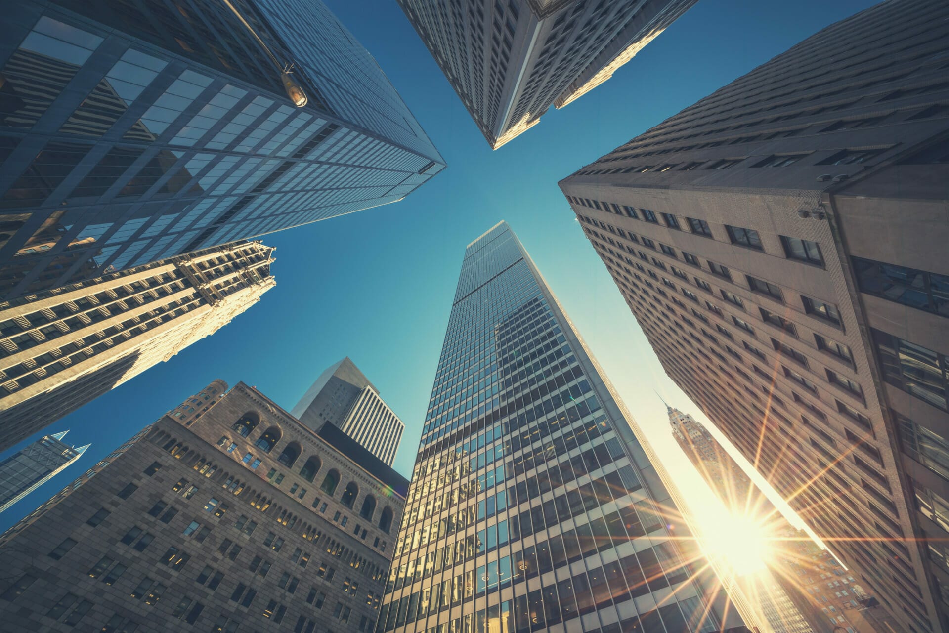 Looking up at tall skyscrapers with the sun shining through the gap between them from a low angle perspective on a clear day, one can almost feel the ambitious energy akin to securing a successful financing round.