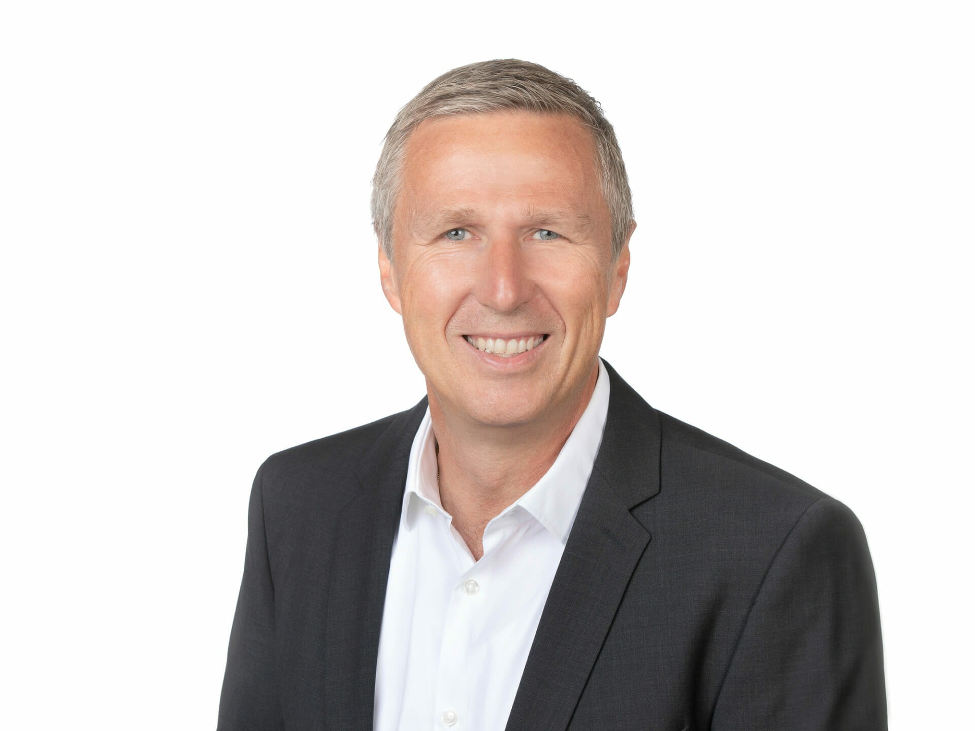 A man with short gray hair, wearing a white shirt and black blazer, smiles at the camera against a plain white background. He exudes the professional elegance of Winterhalter+Fenner standards.