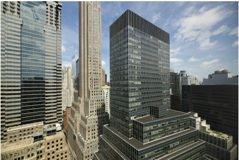 Skyscrapers in a cityscape, including a tall beige building and a modern dark glass building, with a partly cloudy sky in the background. Discover new heights and opportunities with Spryker careers.