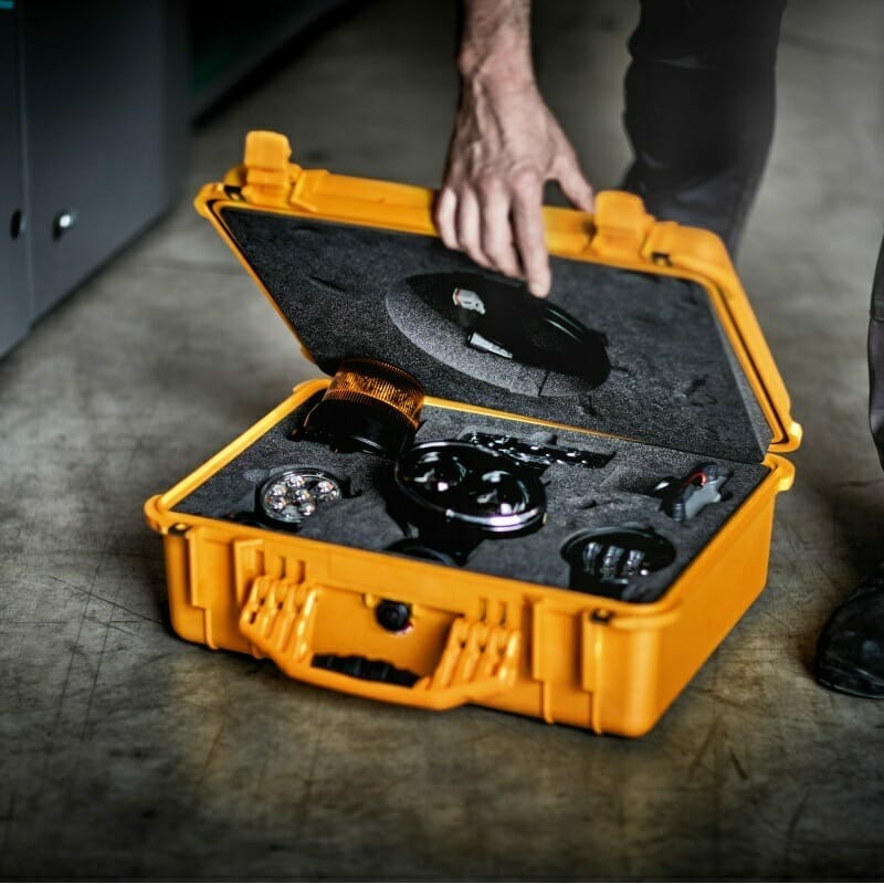 A person opens a yellow protective case containing various electronic devices and components from Spryker on a concrete floor.