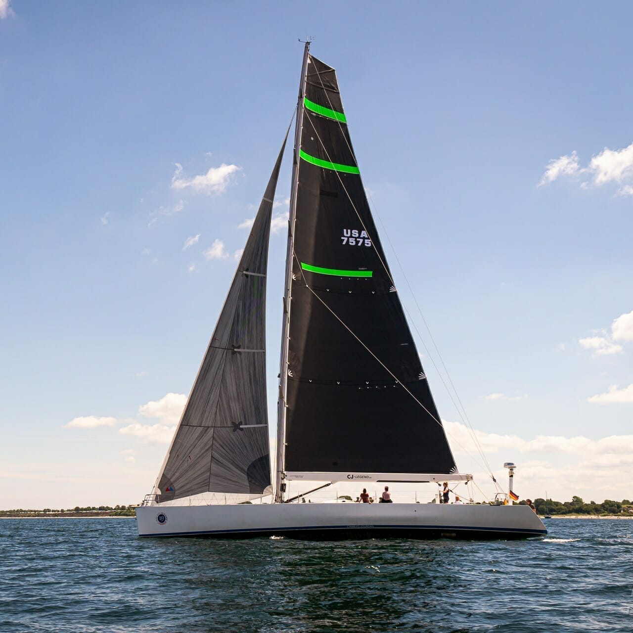 A sailboat with the identifier "USA 797" on its sail glides on open waters under a clear sky with puffy white clouds, embodying the spirit of corporate sailing adventures.