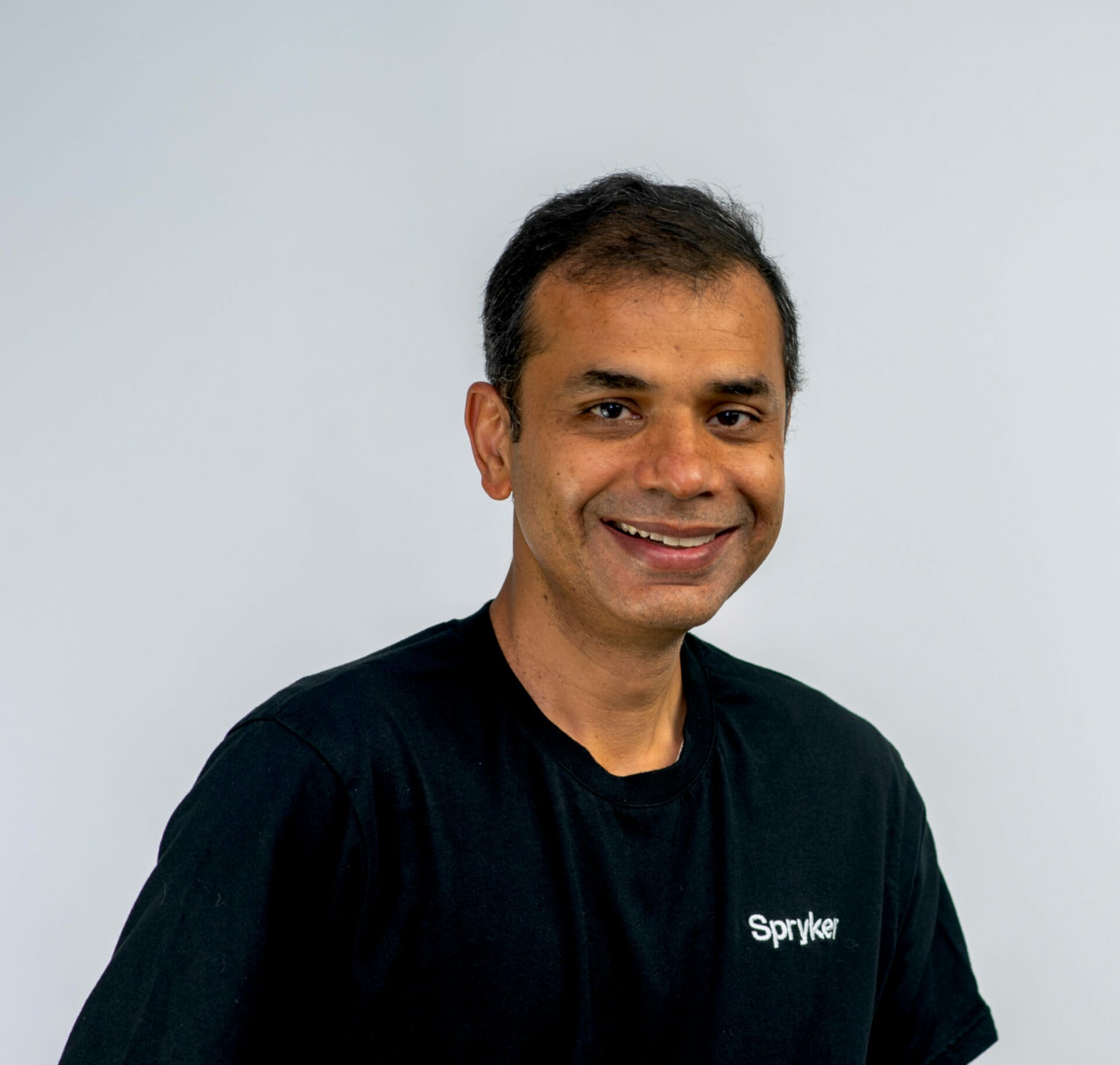 A person wearing a black Spryker t-shirt smiles at the camera against a plain light-colored background, commemorating their experience at Seamless Dubai 2022.