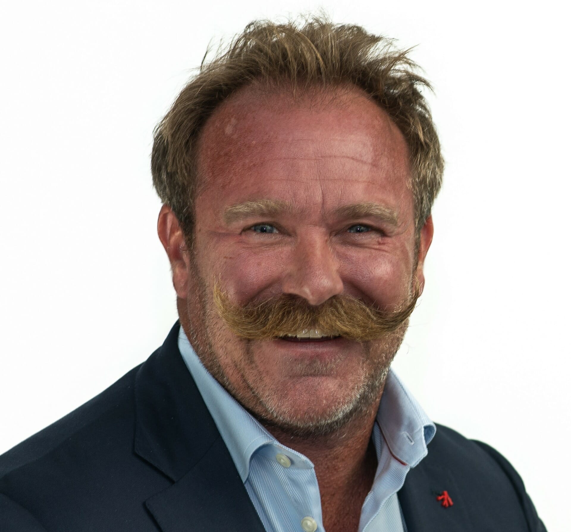 A man with a bushy mustache and short hair smiles at the camera. He is wearing a navy blue blazer over a light blue shirt, exuding professionalism suited for B2B online ventures. The background is plain white, capturing the essence of Chicago's straightforward business approach.