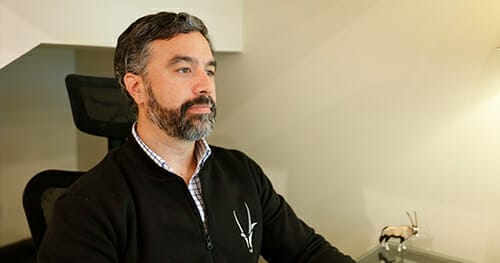 A man with a beard wearing a black sweater sits at a desk with a small animal figurine in the background, perhaps contemplating his next move in his Spryker career.