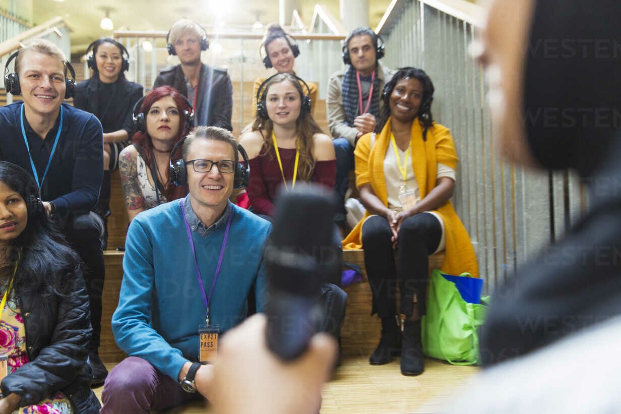 A diverse group of people sitting on steps, wearing lanyards and headphones, listen attentively to a speaker holding a microphone in the foreground at Seamless Dubai 2022.