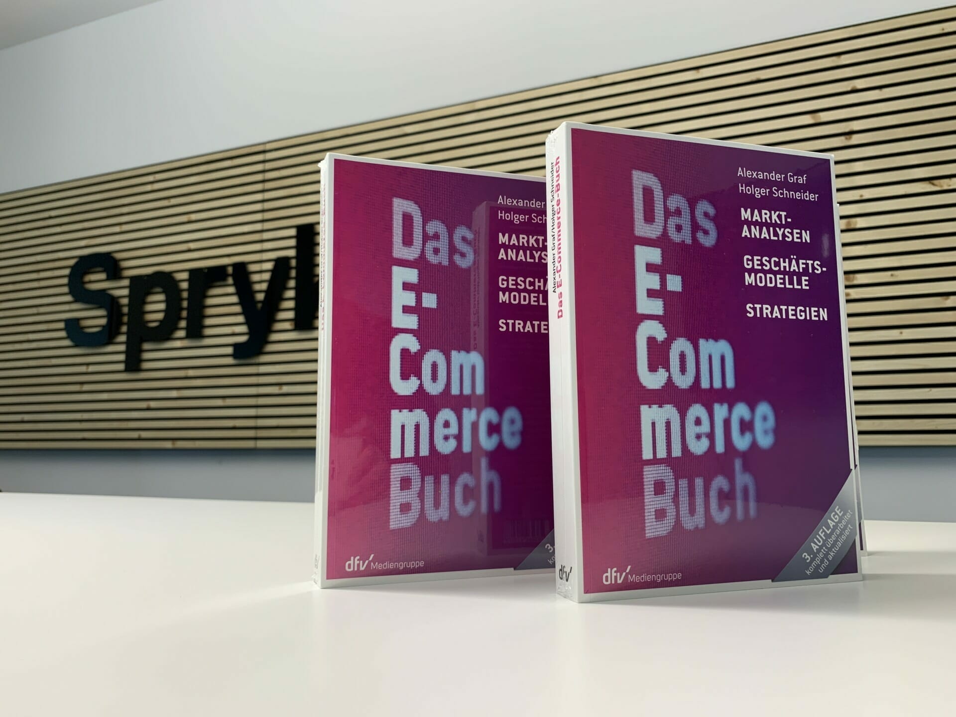 Two copies of a book titled "Das E-Commerce Buch" are placed on a table with a sign labeled "Spryl," showcasing insights from the K5 Konferenz 2022.