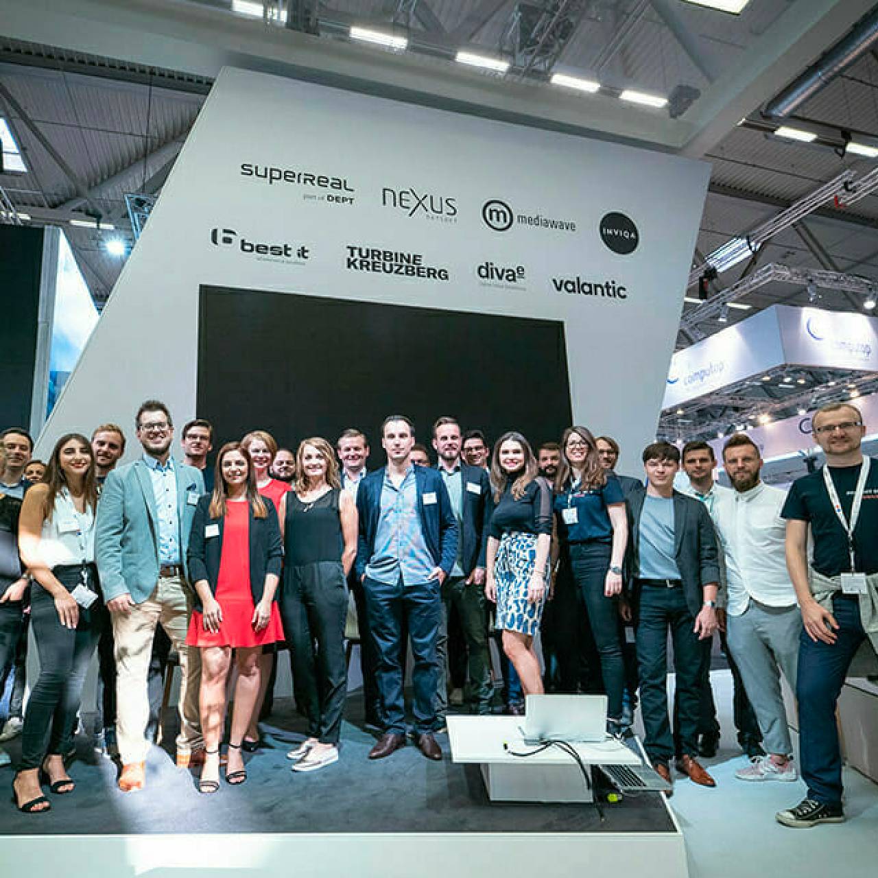 A group of people posing for a photo in front of a display showcasing various company logos at the K5 Konferenz 2022.