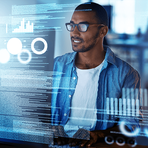 Man wearing glasses uses a computer with graphical data overlays and charts displayed on the screen, interacting seamlessly with the API (Application Programming Interface).