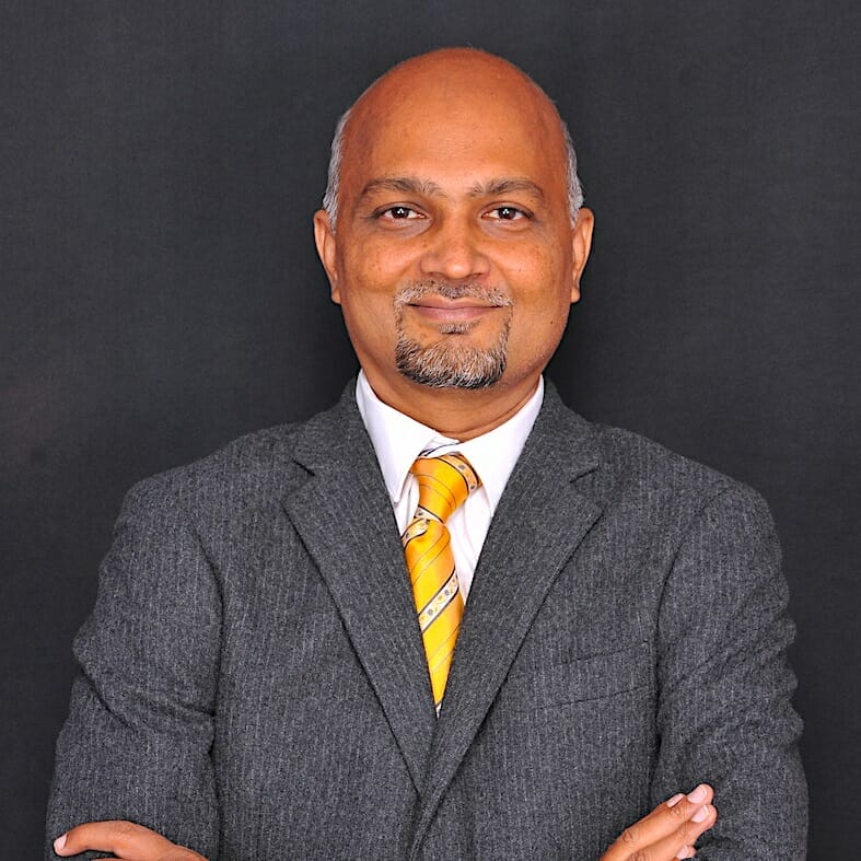 A bald man with a goatee, dressed in a grey suit and a yellow striped tie, stands confidently with his arms crossed against a black background, embodying the sharp professionalism of Asia's eCommerce sector.