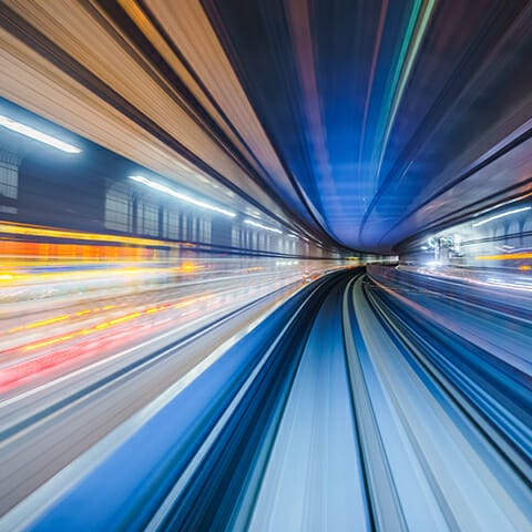 A dynamic, abstract image showing bright, colorful streaks of light and motion blur in a tunnel evokes a sense of high speed and futuristic transport, mirroring the seamless integration seen in composable commerce.