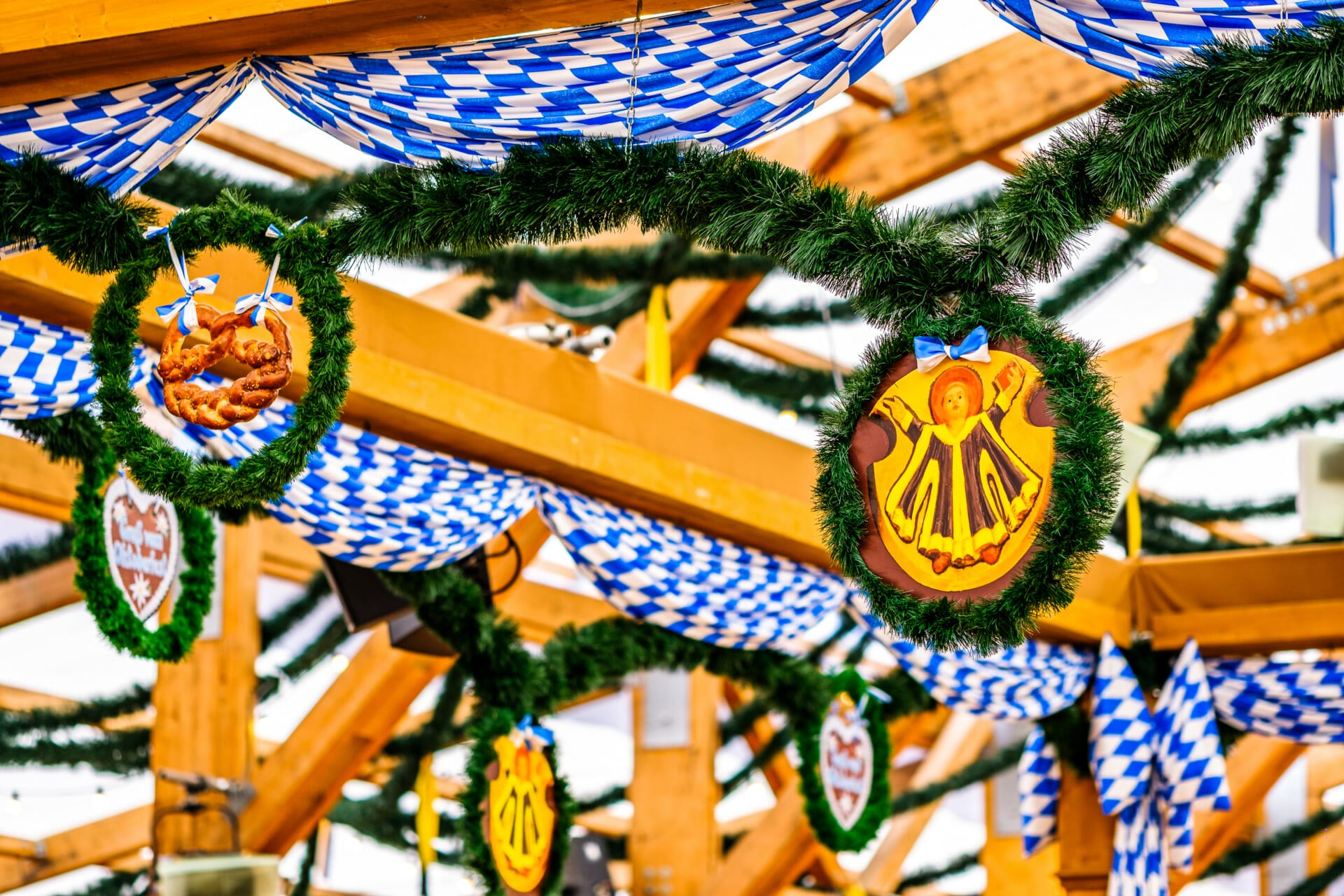 Oktoberfest decorations with blue and white checkered flags and wreaths hang from a wooden structure, creating an atmosphere reminiscent of a B2B-Wiesn celebration.