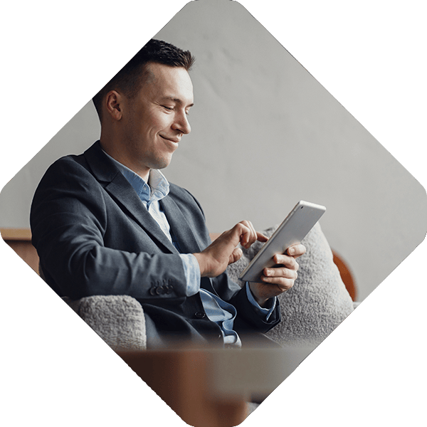 A man in a suit sits on a couch, using a tablet and smiling as he navigates the commerce platform.