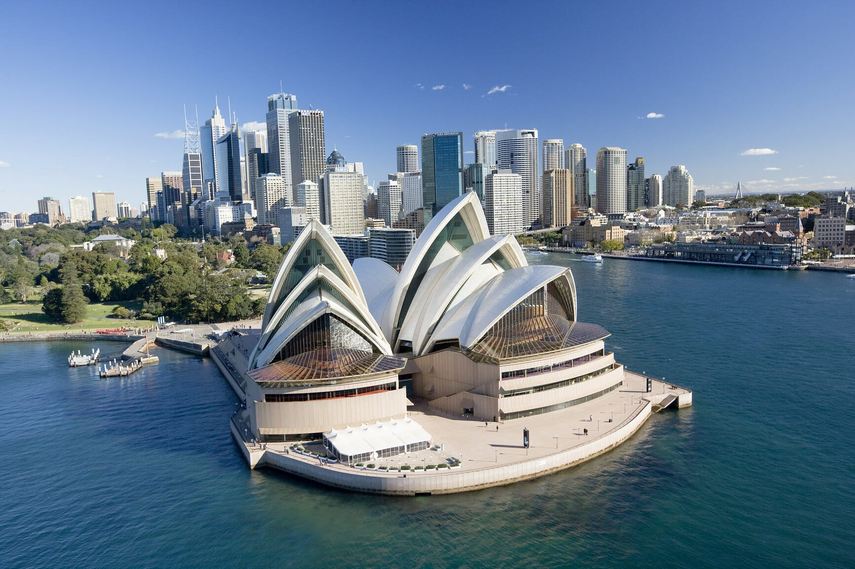 Aerial view of the Sydney Opera House with its distinct sail-like design, seamlessly set against the backdrop of Sydney's city skyline and waterfront.