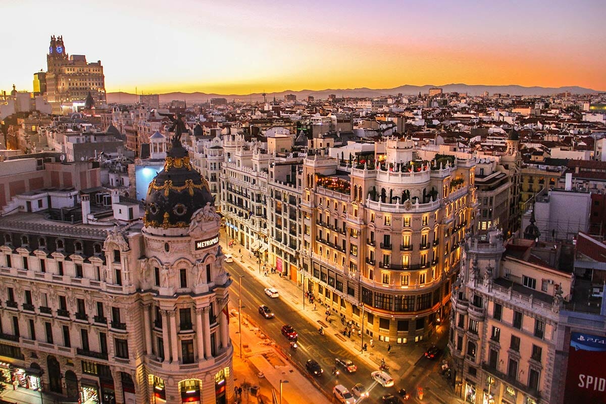 Aerial view of a bustling cityscape at sunset in Saudi Arabia, with historical buildings, a prominent dome structure, and seamless street lights illuminating the streets below.