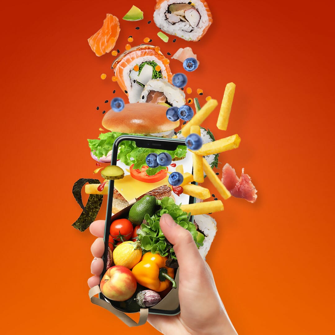 A hand holds a smartphone with various foods, such as fruits, vegetables, sushi, and fries, appearing to spill out of the screen against an orange background – showcasing the vibrant selection available at an Australian online grocery.