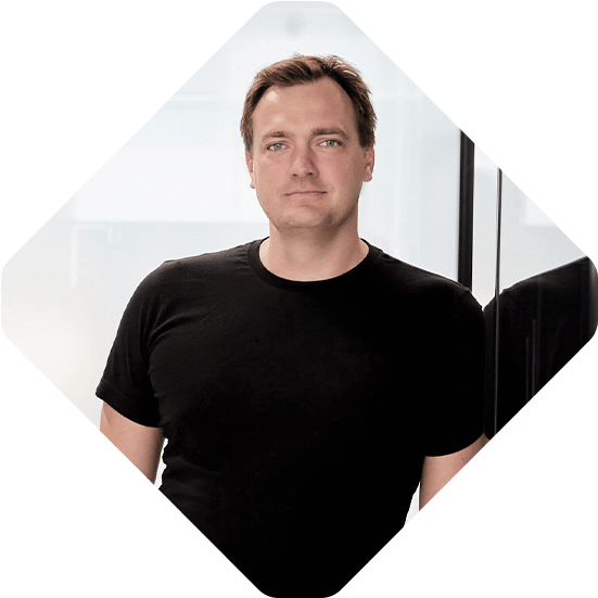 A person in a black t-shirt stands in an office setting with glass walls, preparing for a Commerce Talks podcast.