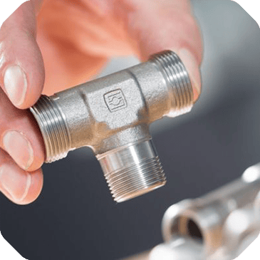 A hand holds a metal T-shaped plumbing fitting with threaded ends against a blurred background, highlighting the essential tools showcased on the Customer Overview Page.