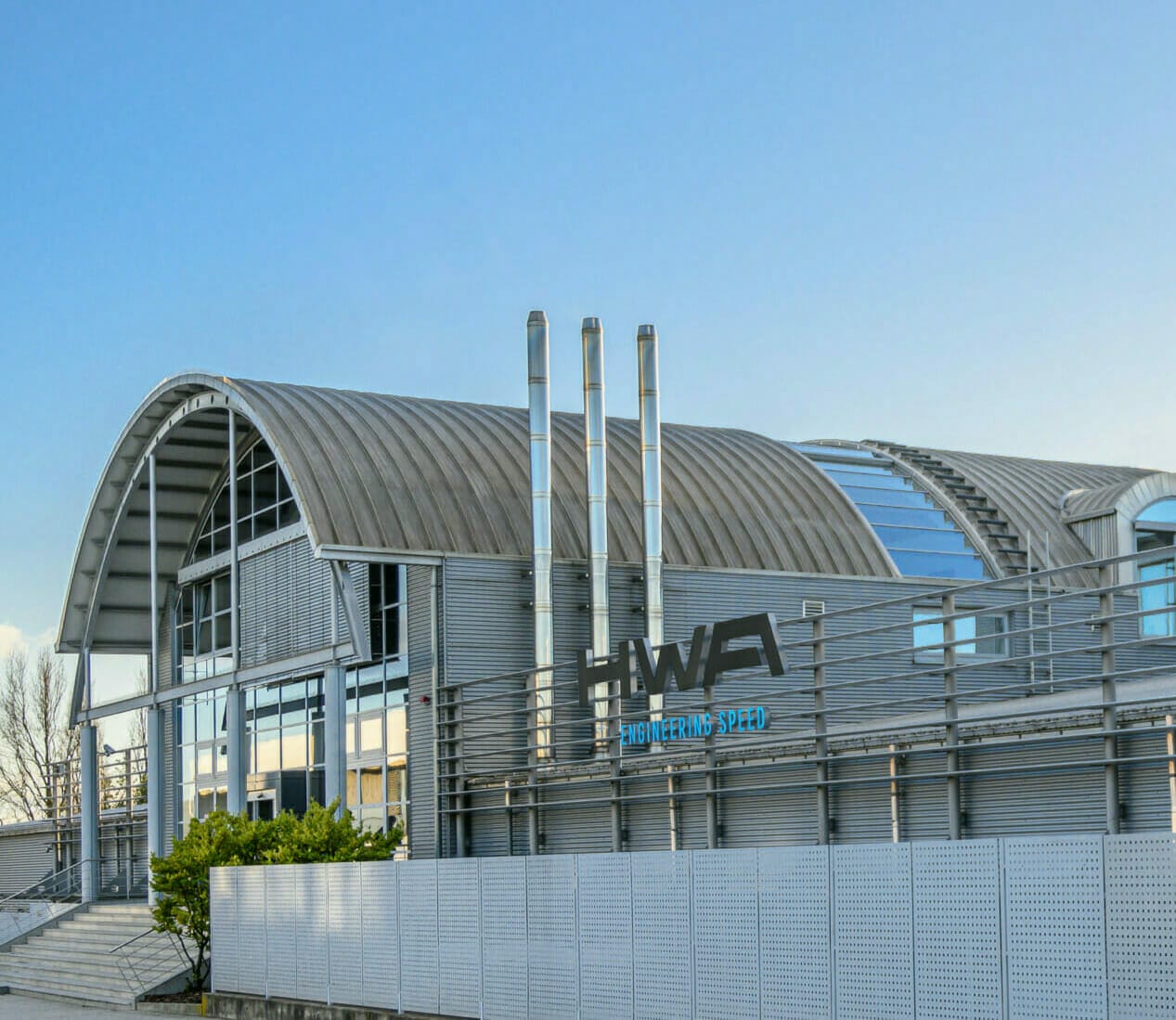 A modern industrial building with curved metal roofing, labelled "HWA Engineering" on the front, epitomizes digital success. The structure features large windows, metal chimneys, and a clear sky background.