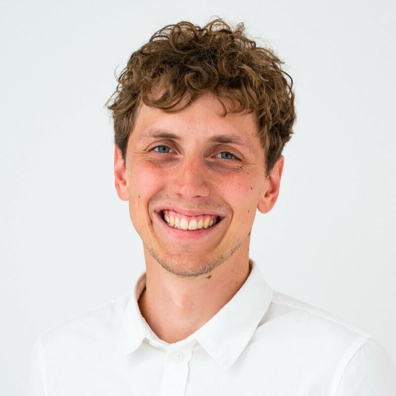 A man with curly hair and a white shirt is smiling at the camera, embodying the approachable spirit of our customer advisory board, against a plain white background.