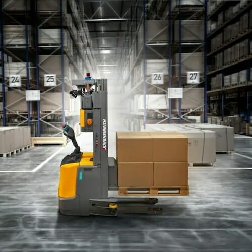 A Jungheinrich forklift, driven by one of our spryker customers, maneuvers a pallet of cardboard boxes through a large warehouse with numbered racks.