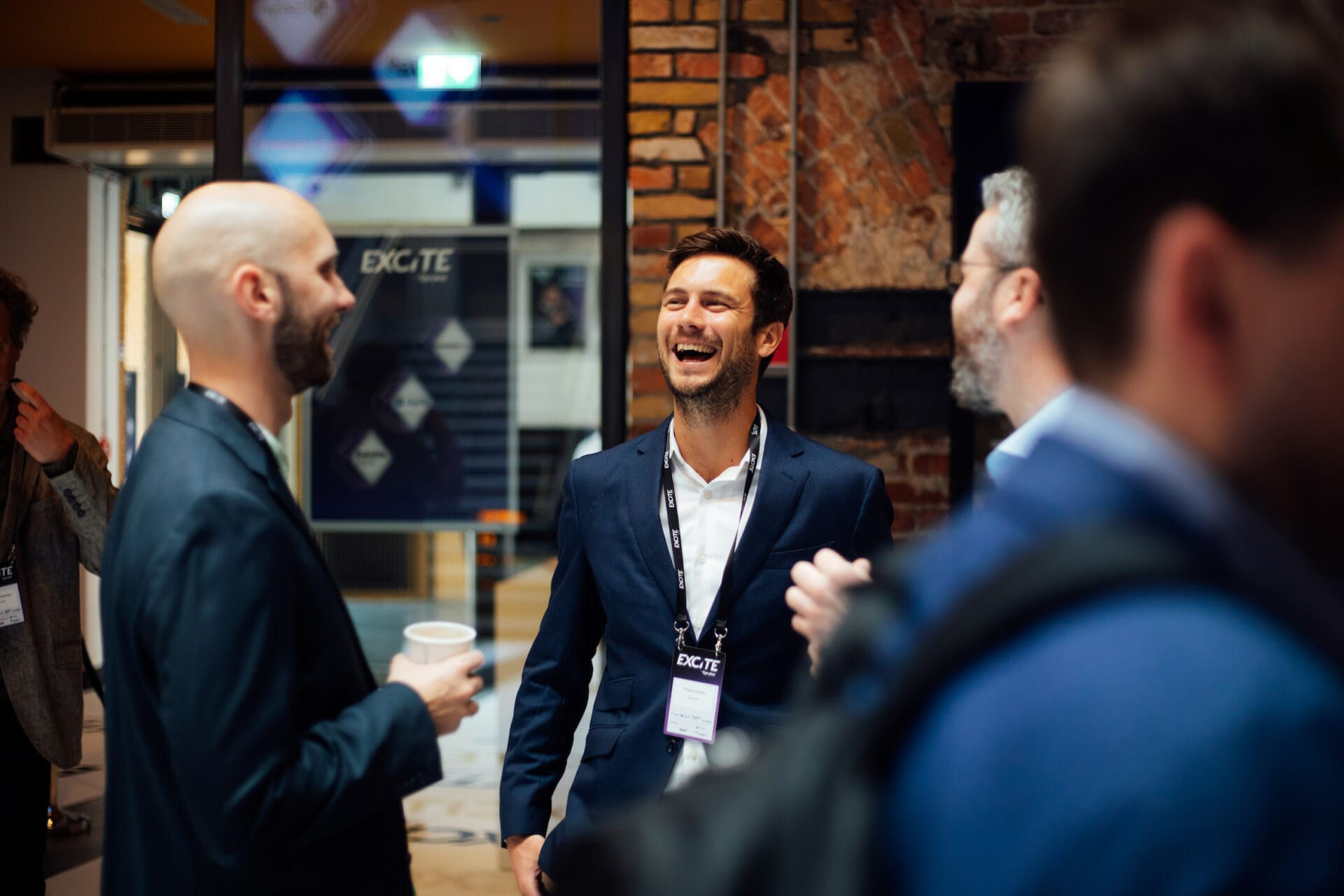 Three men in business attire are engaged in a lively conversation at what appears to be the Seamless Middle East 2023 event, with one man laughing. A fourth person is partially visible in the foreground.