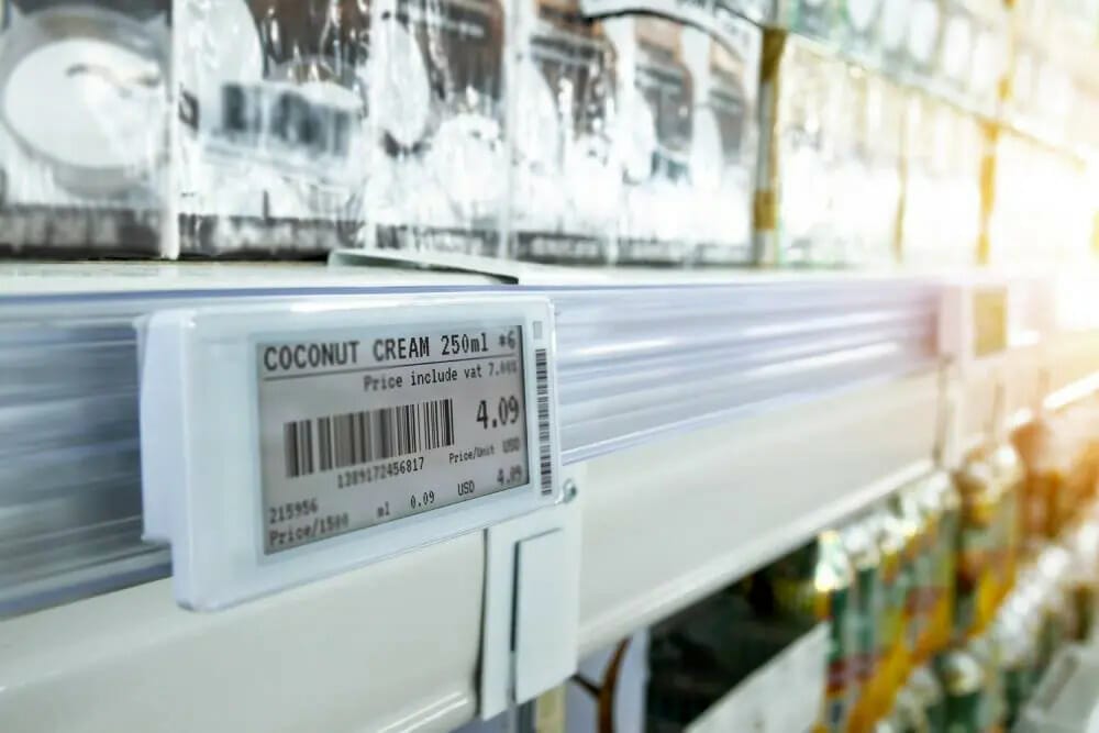 Close-up of a headless digital price tag displaying the price of coconut cream on a supermarket shelf, with the packaging visible in the background.