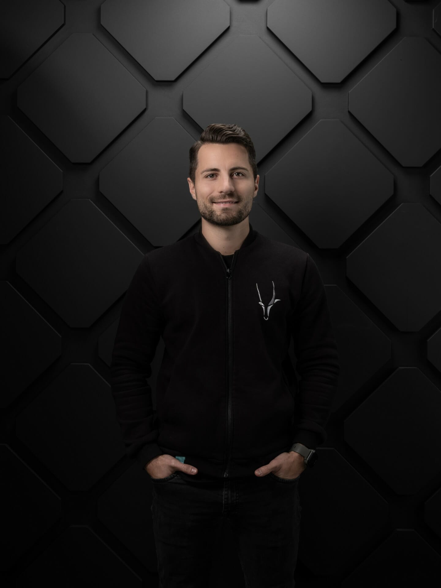 A person with short hair, wearing a black jacket with a K5 Konferenz 2023 logo, stands in front of a textured black wall with a geometric pattern.