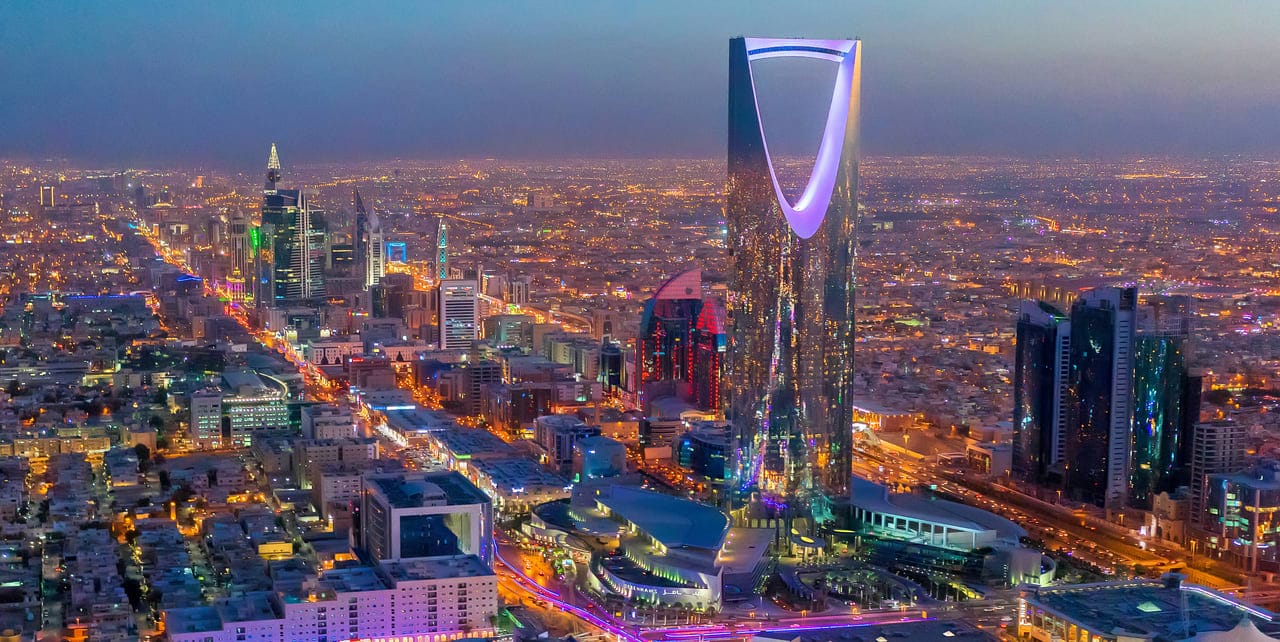 Aerial view of Riyadh at dusk, seamlessly showcasing the illuminated Kingdom Centre Tower and surrounding cityscape, capturing the essence of Saudi Arabia 2023.