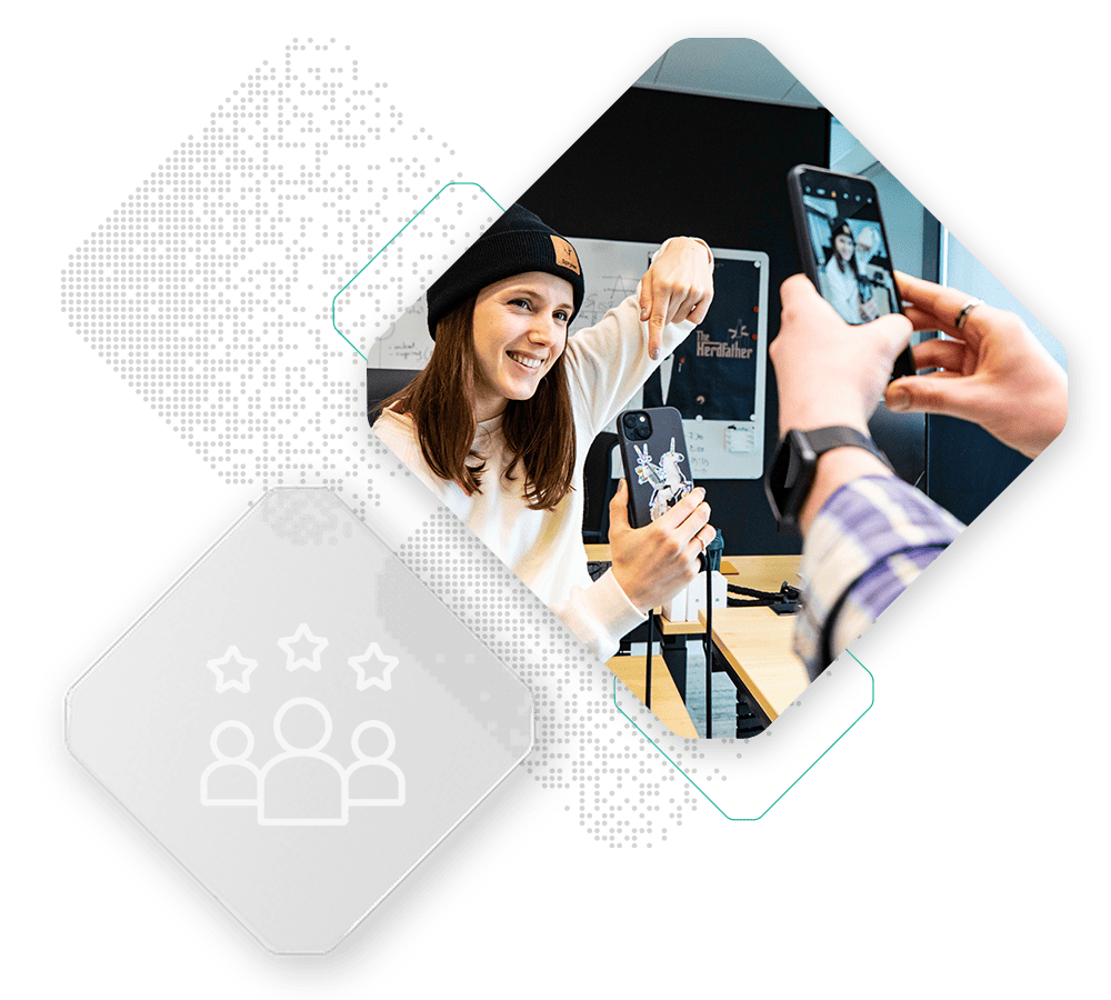 A person wearing a black beanie and white shirt is smiling and pointing at their phone, while another person captures a photo of them using a smartphone. Icon of a group with stars overlayed, representing the collaborative spirit in our b2b suite.