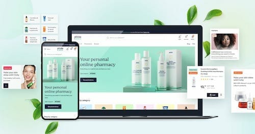 A laptop and a smartphone display the homepage of an online pharmacy, powered by Spryker. Surrounding them are various product images and customer reviews. Green leaves are scattered in the background.