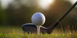 Close-up of a golf club poised to hit a golf ball placed on a tee, against a blurred outdoor background highlighting the commitment to sustainable commerce in sports.