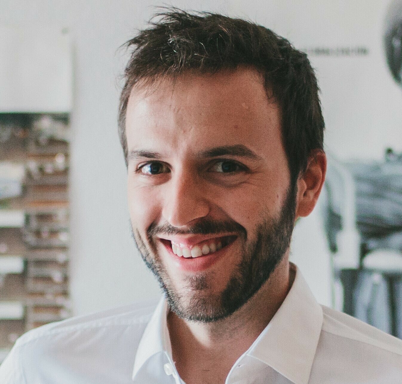 A man with a beard and short hair smiles while wearing a white shirt, standing indoors with a blurred background, likely thinking about digital transformation strategies for manufacturers.