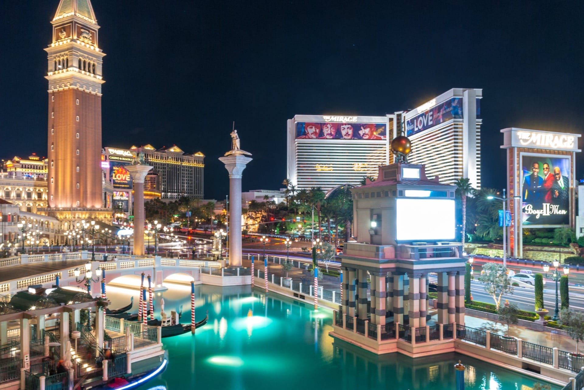 Night view of the Las Vegas Strip featuring illuminated hotels and casinos. Prominent landmarks include replicas of the Venetian Tower and Statue of Liberty with a view of a tranquil canal, setting the stage perfectly for CES 2024.