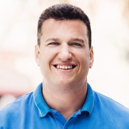 Man in blue polo shirt smiling at the camera with a backdrop reminiscent of Spryker EXCITE 2024's vibrant outdoor setting.