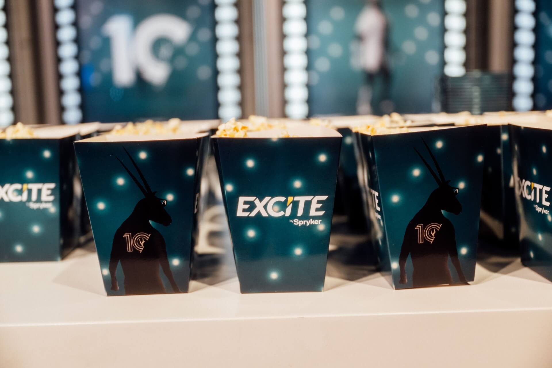 Rows of popcorn boxes labeled "EXCITE" are arranged on a table, reflecting seamless supply chain management.