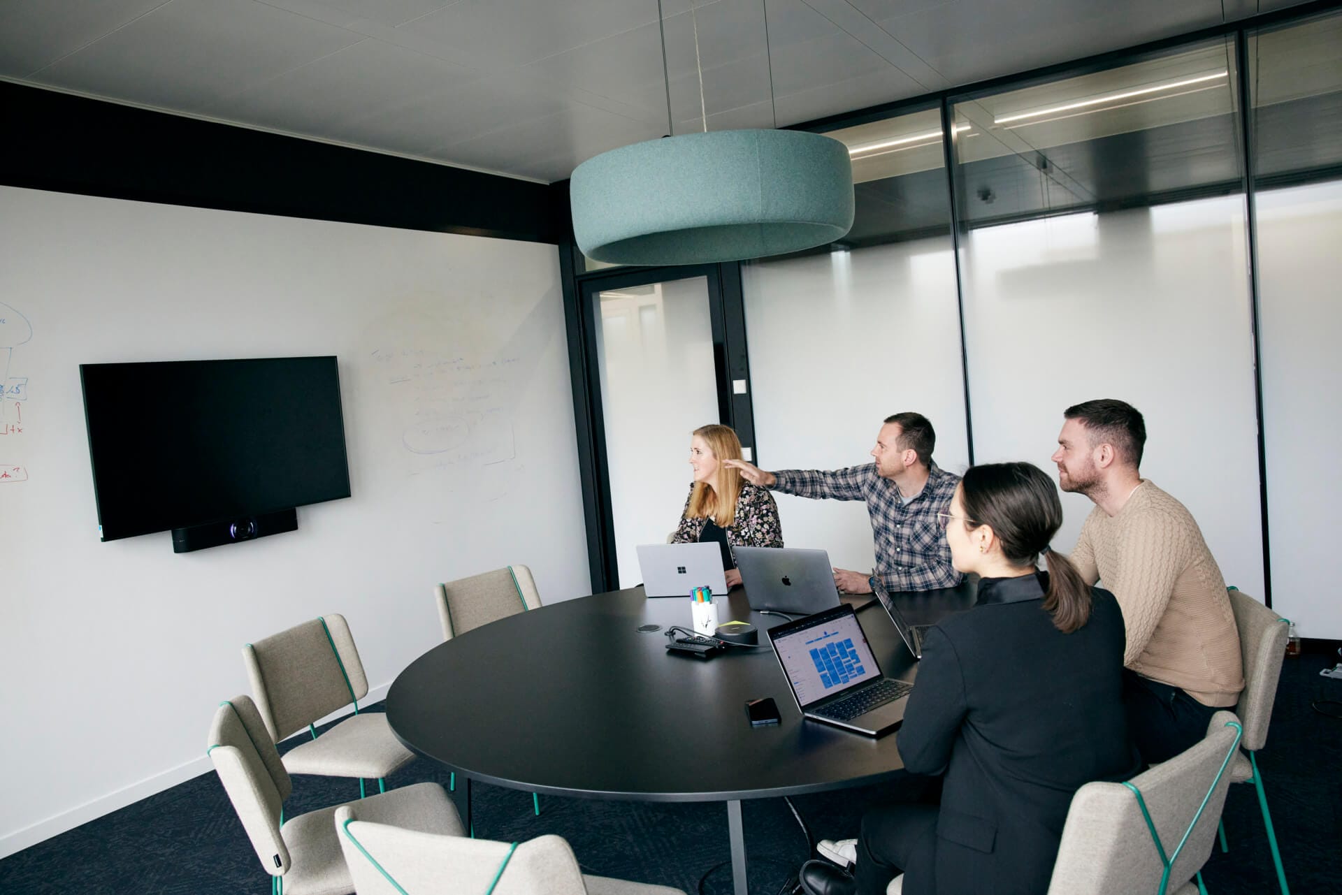 Four people in a conference room watch a presentation about Stripe on a wall-mounted screen. Laptops are open on the round table.