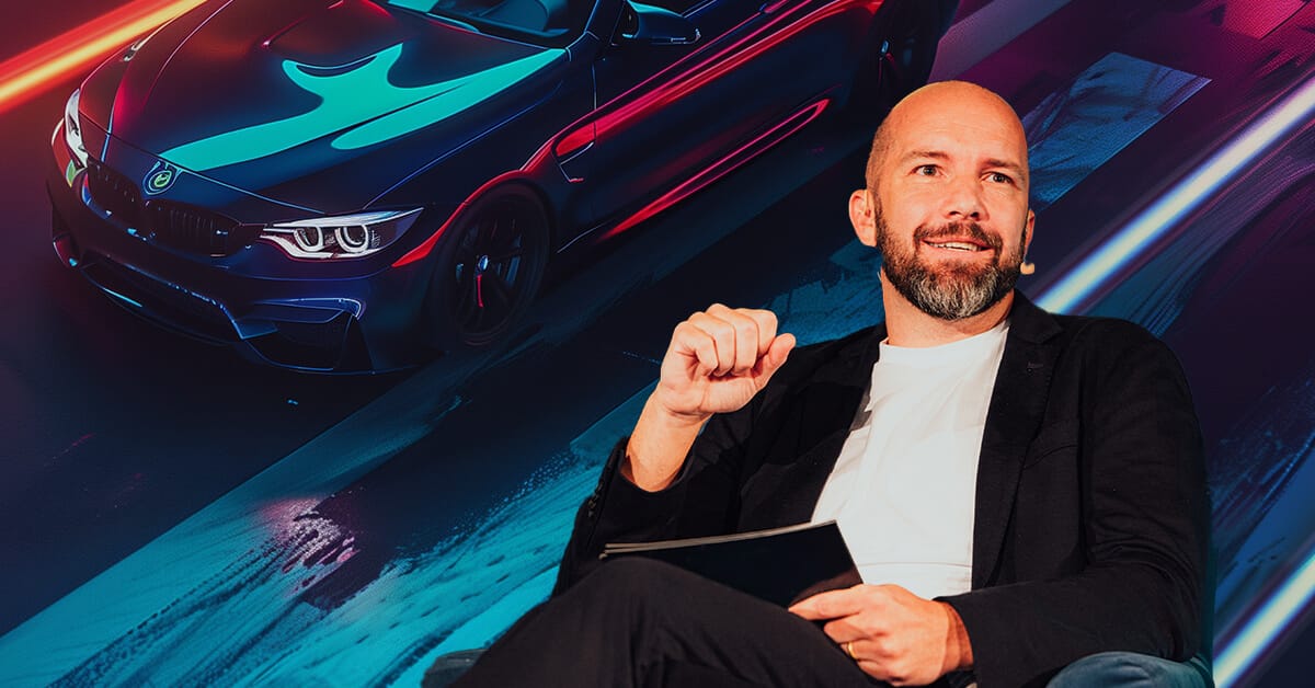 A man in a blazer and white shirt speaks, with a vibrant image of a sports car in motion in the background, capturing the dynamic essence akin to Gartner's visionary insights.