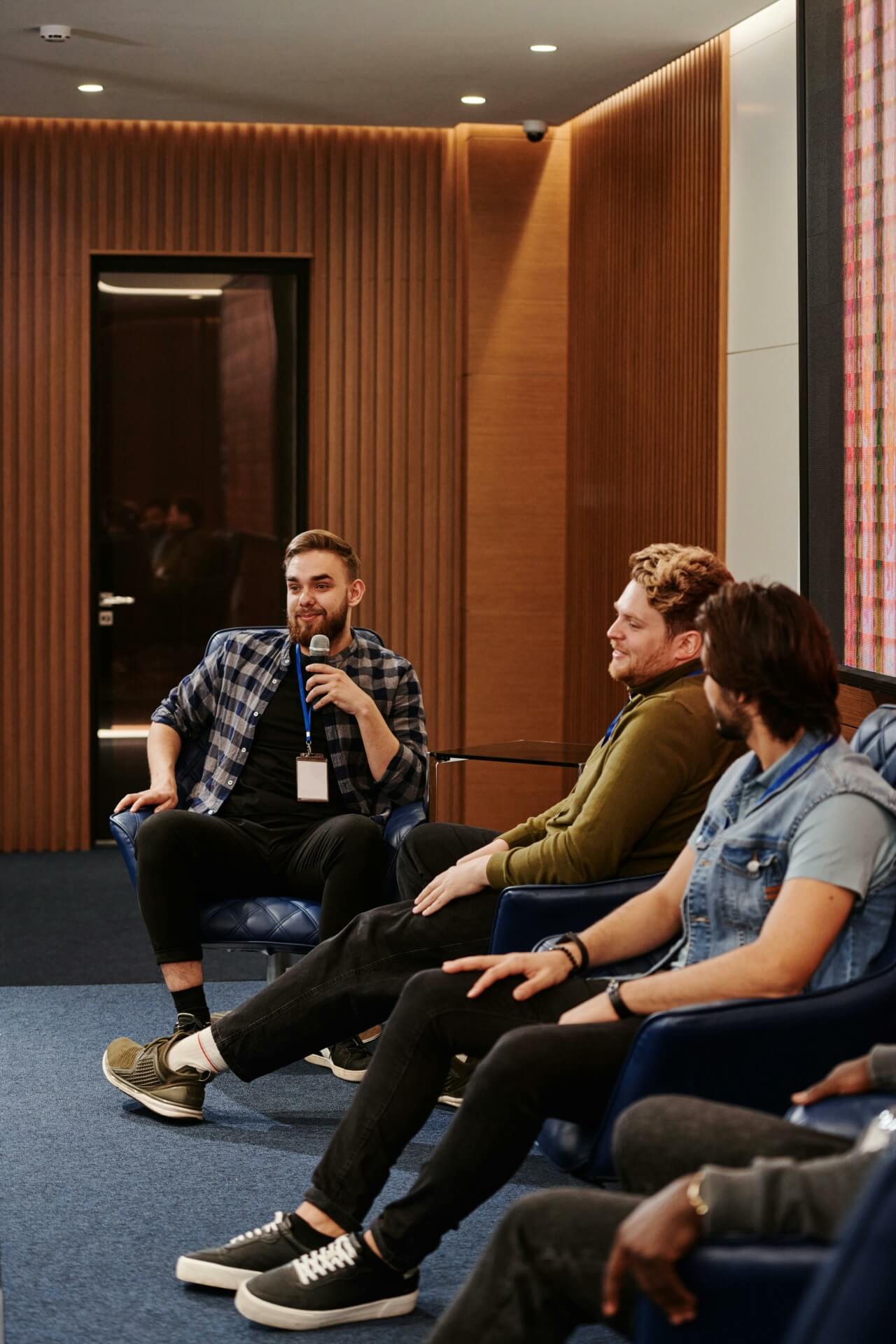 In a modern room, four individuals sit on chairs, deeply engaged in a discussion. As one person holds a microphone, the others listen attentively, embodying the collaborative spirit of a Side Event at B2B Online Europe 2024.