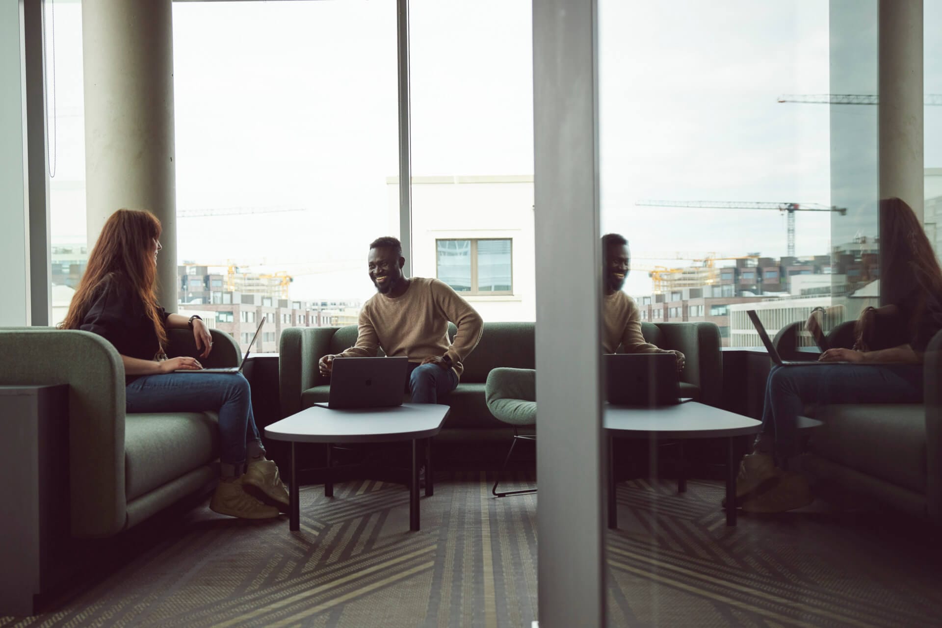 Two people sitting and talking in a modern office lounge with a window reflecting their image, as they discuss the latest Gartner Magic Quadrant report. Outside, the hum of a construction site adds a dynamic backdrop to their engaging conversation.