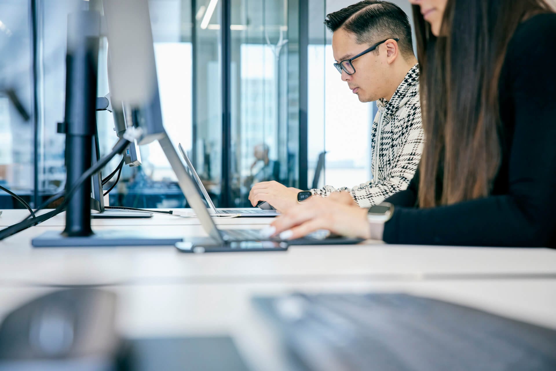 Two people immersed in their work on laptops at a desk in a modern office, framed by a large window showcasing a breathtaking city view—a scene reminiscent of analyzing the latest Gartner Magic Quadrant.