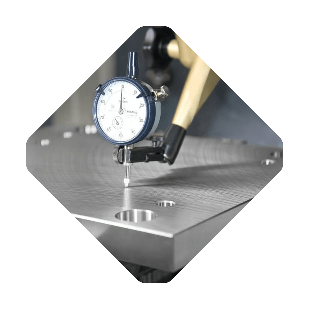 A Meusburger dial indicator measures the surface flatness of a machined metal plate.